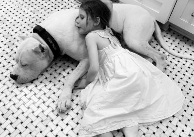 Black-and-white photo of a World Class Dogo Argentino white dog lying on a tiled floor next to a child